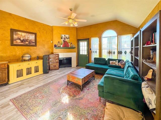 living area with lofted ceiling, a ceiling fan, a tiled fireplace, and wood finished floors