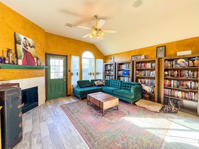 living room with lofted ceiling, visible vents, a tiled fireplace, ceiling fan, and wood finished floors