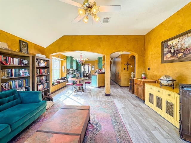 interior space featuring arched walkways, ceiling fan with notable chandelier, visible vents, vaulted ceiling, and light wood finished floors