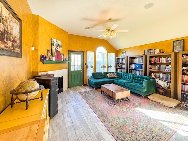 sitting room with visible vents, ceiling fan, vaulted ceiling, wood finished floors, and a tile fireplace