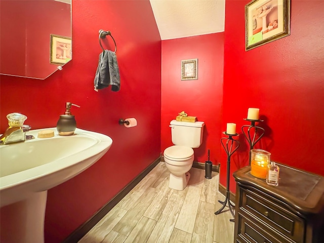 half bath featuring toilet, a sink, baseboards, and wood finished floors