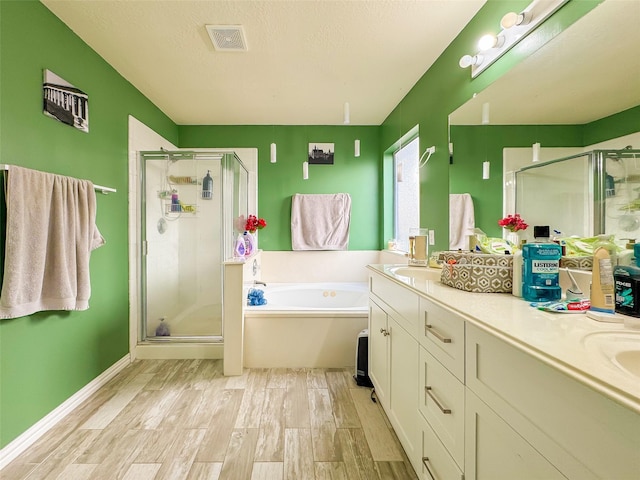 full bath with a textured ceiling, wood finished floors, a bath, double vanity, and a stall shower