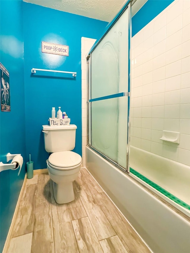 bathroom with toilet, baseboards, combined bath / shower with glass door, and a textured ceiling