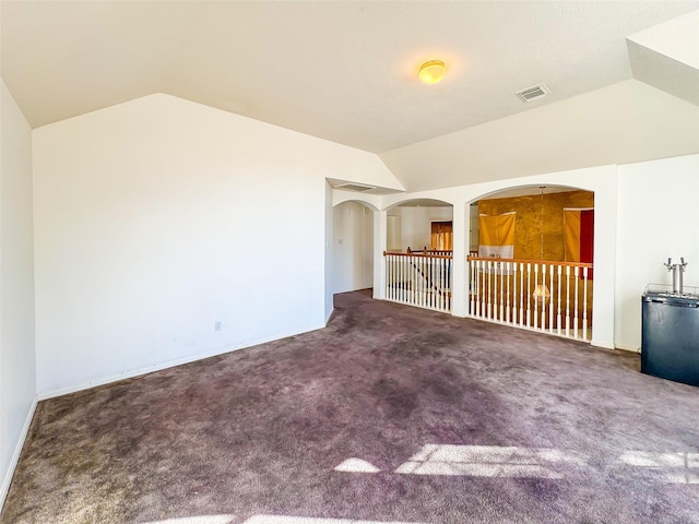 carpeted empty room with lofted ceiling, visible vents, and arched walkways