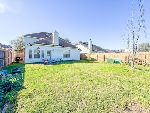 rear view of property featuring a fenced backyard, a chimney, and a lawn