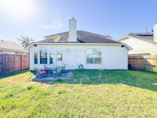 rear view of house featuring a patio, a fenced backyard, a shingled roof, a lawn, and a chimney