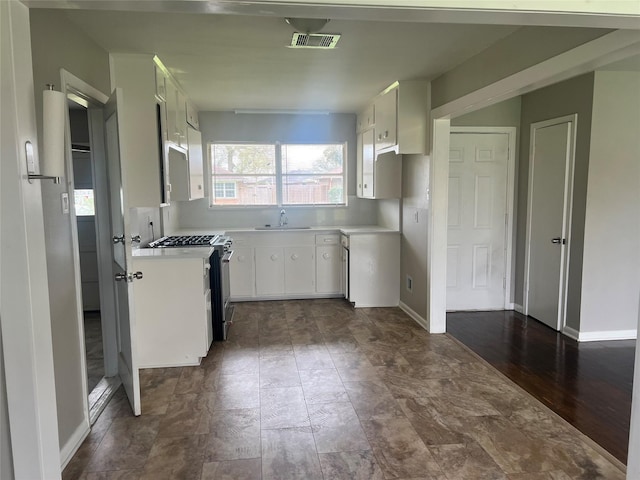 kitchen with stainless steel gas stove, visible vents, white cabinets, light countertops, and a sink