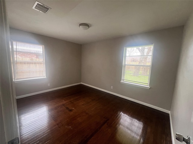 empty room with dark wood-type flooring, visible vents, and baseboards