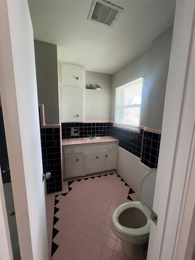 bathroom featuring toilet, a wainscoted wall, visible vents, and tile walls