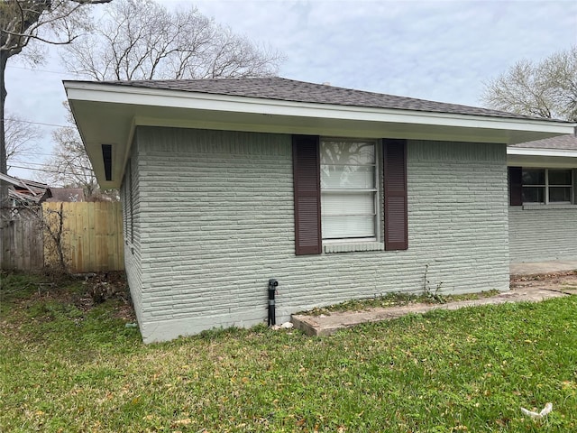 view of side of property with fence, a lawn, and roof with shingles