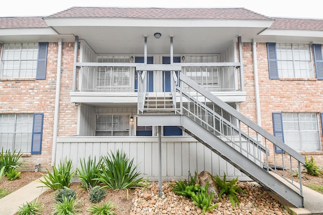 exterior space featuring roof with shingles, brick siding, and stairs