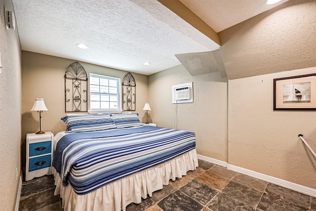 bedroom with a wall mounted air conditioner, a textured wall, a textured ceiling, and baseboards