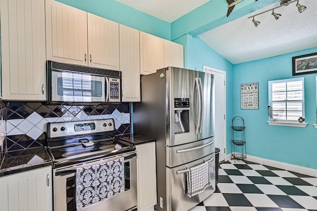 kitchen featuring baseboards, decorative backsplash, tile patterned floors, vaulted ceiling, and stainless steel appliances