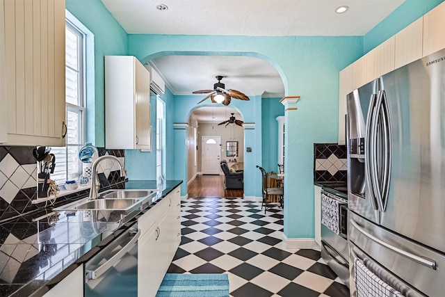 kitchen featuring arched walkways, a sink, appliances with stainless steel finishes, backsplash, and tile patterned floors