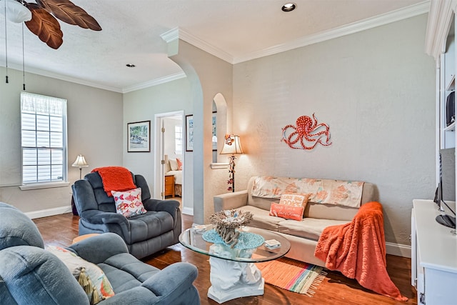 living room featuring baseboards, arched walkways, a ceiling fan, and ornamental molding