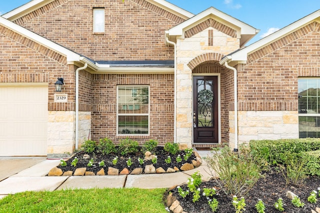 entrance to property featuring a garage, stone siding, and brick siding