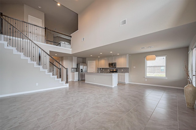 unfurnished living room featuring light tile patterned flooring, a sink, visible vents, baseboards, and stairway