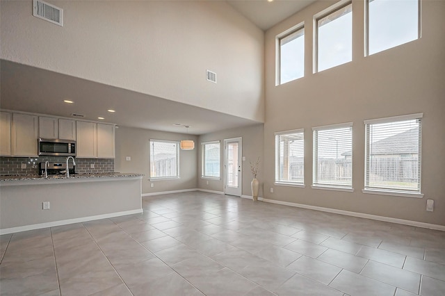 unfurnished living room featuring light tile patterned floors, a sink, visible vents, and baseboards