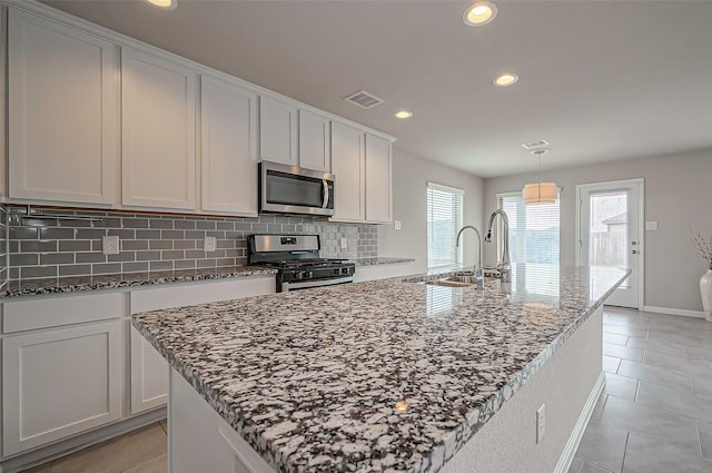 kitchen featuring a sink, appliances with stainless steel finishes, tasteful backsplash, dark stone countertops, and a center island with sink