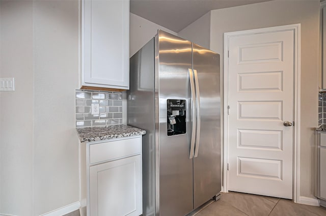 kitchen with light tile patterned floors, white cabinetry, stainless steel fridge with ice dispenser, light stone countertops, and tasteful backsplash