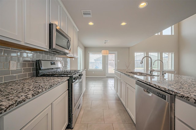 kitchen featuring light tile patterned floors, stainless steel appliances, decorative backsplash, stone countertops, and a sink