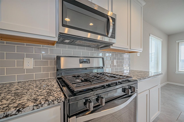 kitchen featuring stone countertops, gas stove, stainless steel microwave, and white cabinetry