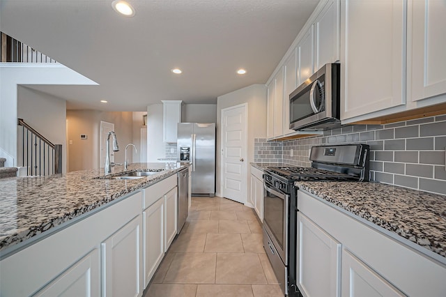 kitchen with stainless steel appliances, stone counters, a sink, and white cabinetry