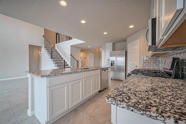 kitchen featuring backsplash, light stone countertops, a kitchen island with sink, stainless steel appliances, and a sink