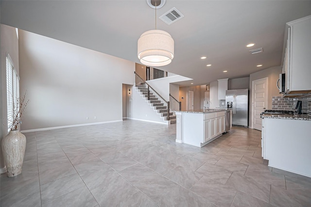 kitchen with light stone counters, stainless steel appliances, a sink, open floor plan, and tasteful backsplash