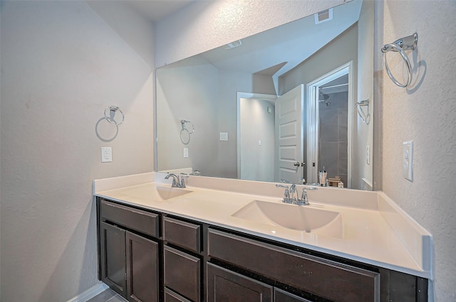 full bath with a shower, a textured wall, a sink, and double vanity