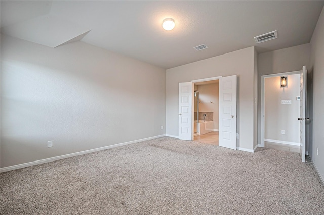 unfurnished bedroom featuring light colored carpet, visible vents, ensuite bath, and baseboards