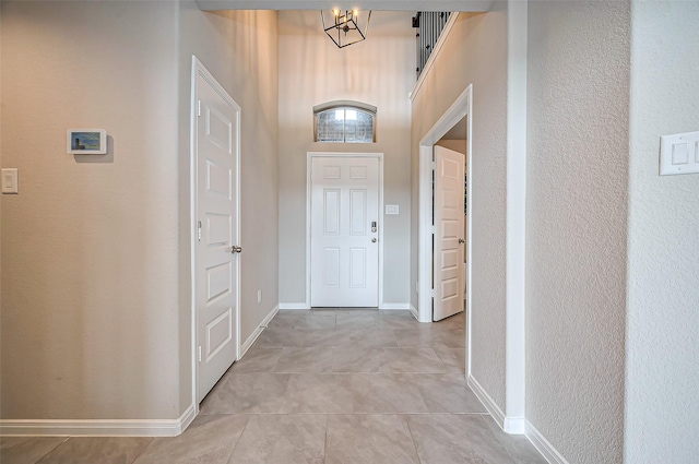 interior space featuring light tile patterned floors, a high ceiling, baseboards, and a chandelier