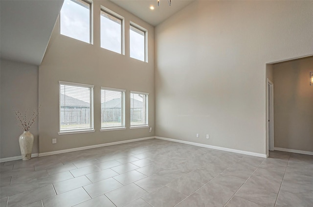 spare room featuring light tile patterned floors, a high ceiling, and baseboards