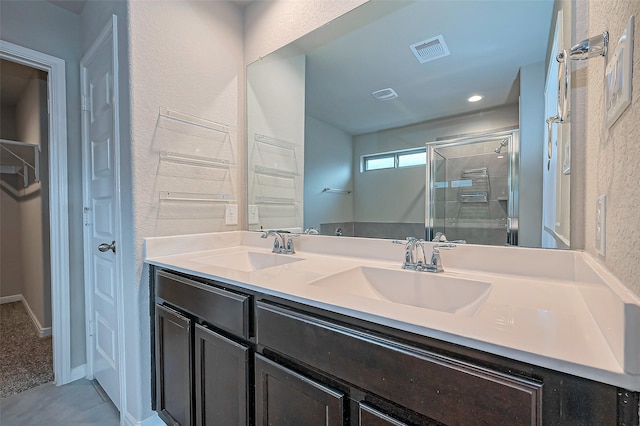 full bathroom featuring visible vents, a sink, a shower stall, and double vanity