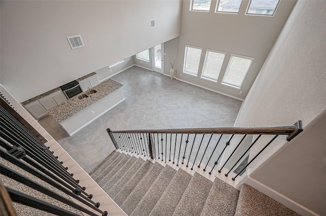 staircase featuring baseboards, visible vents, plenty of natural light, and a high ceiling