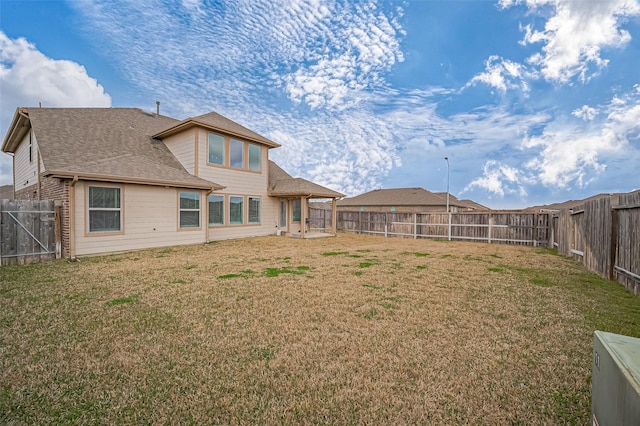 rear view of house featuring a fenced backyard, a shingled roof, and a yard