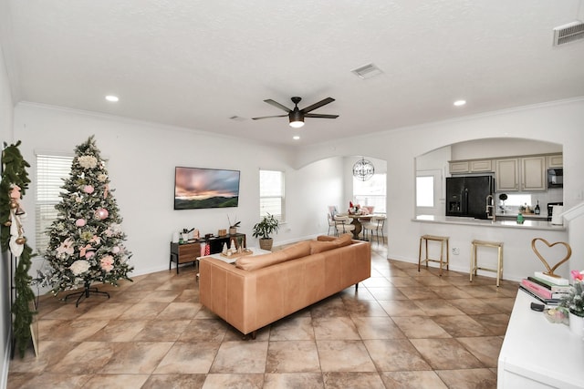 living area with visible vents, arched walkways, baseboards, ceiling fan, and crown molding