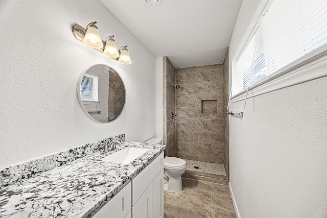 bathroom featuring baseboards, tiled shower, vanity, and toilet