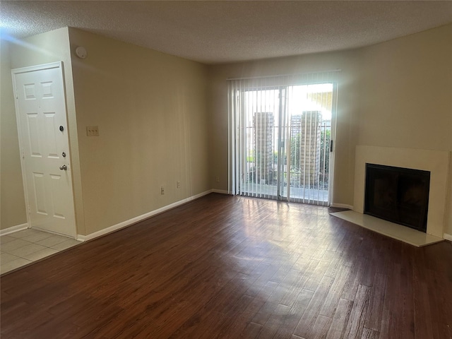 unfurnished living room featuring a textured ceiling, a fireplace, baseboards, and wood finished floors