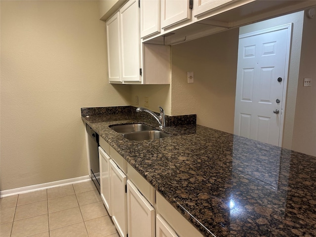 kitchen featuring light tile patterned floors, white cabinets, a sink, dark stone counters, and baseboards