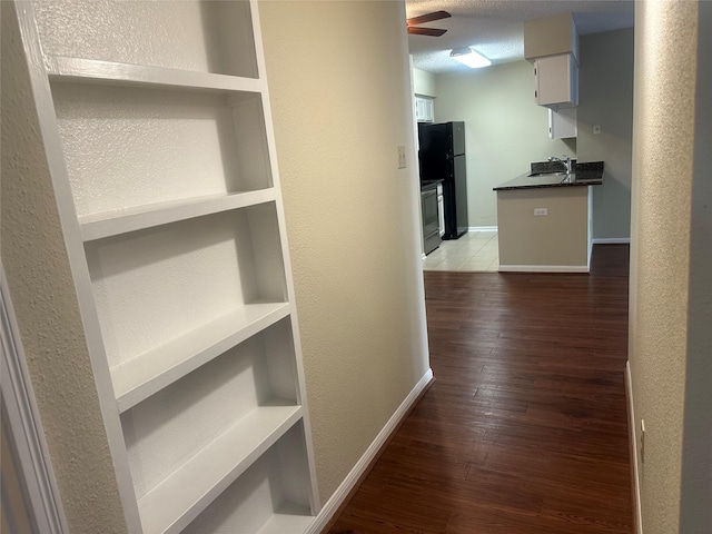 hall with a sink, a textured wall, wood finished floors, and baseboards