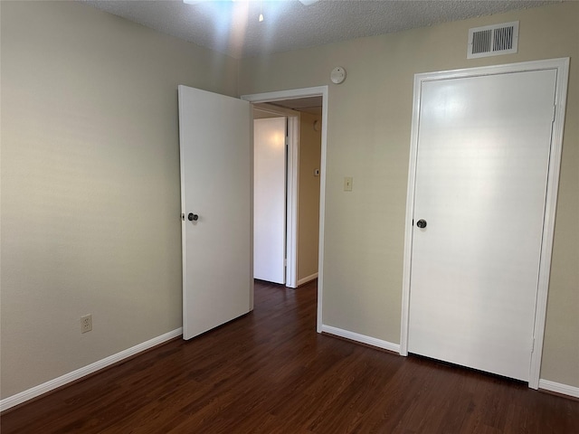 unfurnished bedroom with dark wood-style floors, visible vents, a textured ceiling, and baseboards