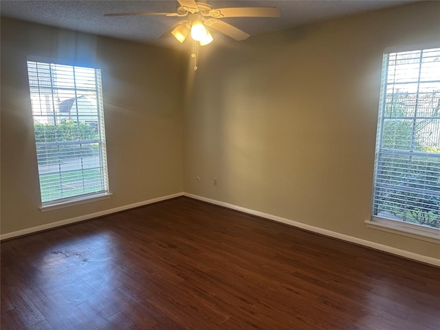 spare room with ceiling fan, baseboards, dark wood-type flooring, and a wealth of natural light