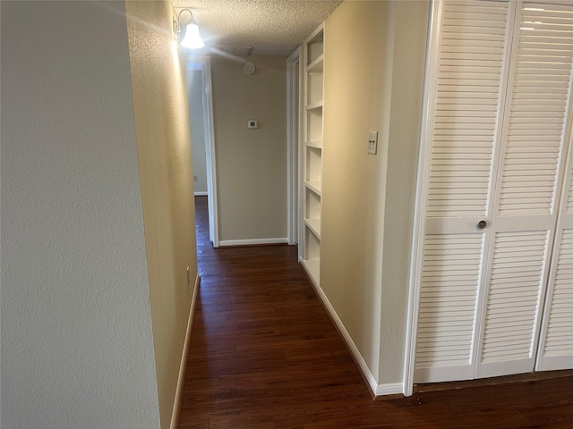 corridor featuring a textured ceiling, a textured wall, dark wood-type flooring, and baseboards