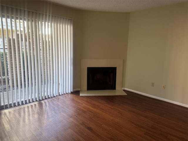 unfurnished living room featuring a large fireplace, a textured ceiling, wood finished floors, and baseboards