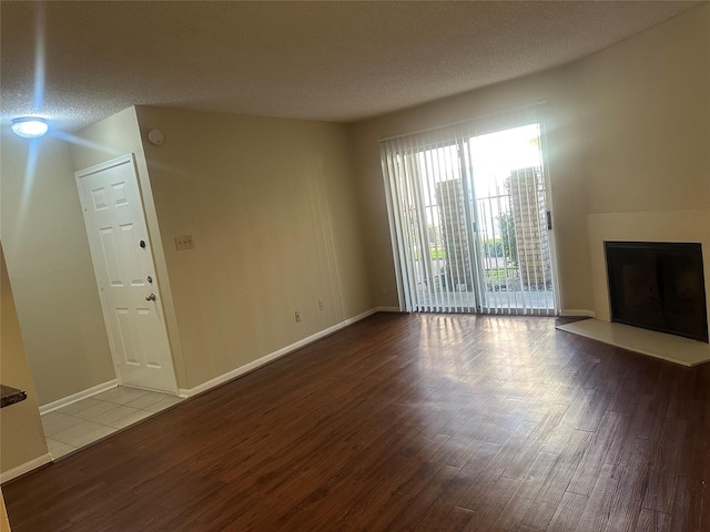 unfurnished living room featuring a textured ceiling, a fireplace with raised hearth, and wood finished floors