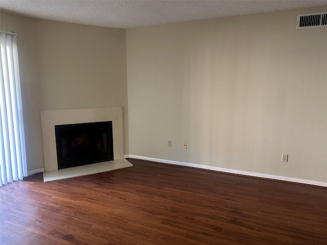 unfurnished living room featuring a fireplace with raised hearth, a textured ceiling, dark wood-type flooring, visible vents, and baseboards