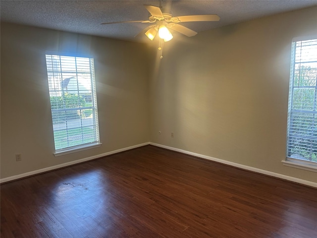 spare room featuring dark wood-style floors, a healthy amount of sunlight, a textured ceiling, and baseboards