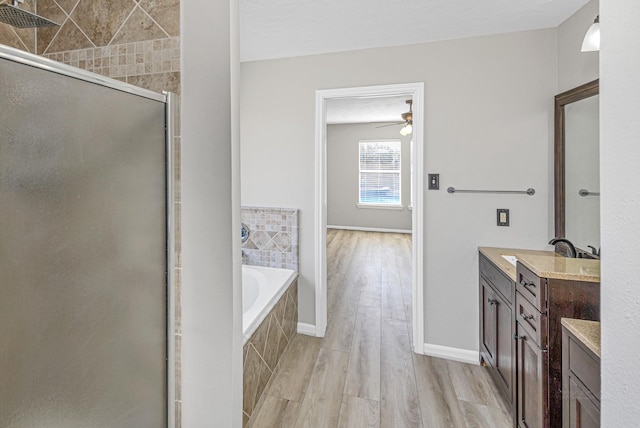 bathroom with a ceiling fan, vanity, a shower stall, wood finished floors, and tiled tub