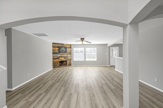 unfurnished living room with a ceiling fan, visible vents, a stone fireplace, and light wood finished floors